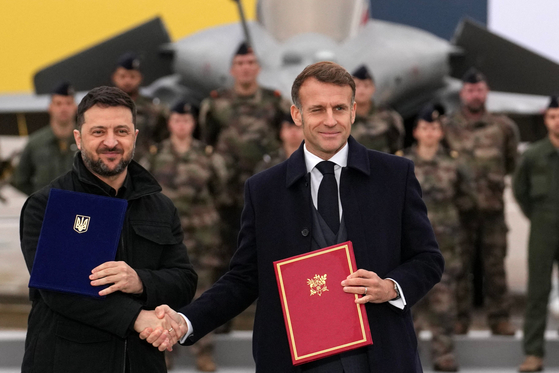 17日、フランスのビラクブレ空軍基地でフランスのマクロン大統領（右）とウクライナのゼレンスキー大統領が合意書署名後に握手している。両首脳はウクライナの戦闘機運用と防空能力強化に向けた武器協定を締結し、ゼレンスキー大統領はこれを「歴史的」と評価した。［写真 AFP＝聯合ニュース］