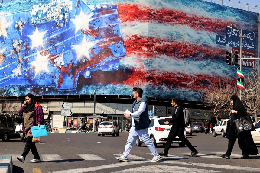 17日、イランのテヘランで米空母が攻撃を受ける場面の反米宣伝ポスター看板の前を市民が歩いている。 ［AFP＝聯合ニュース］