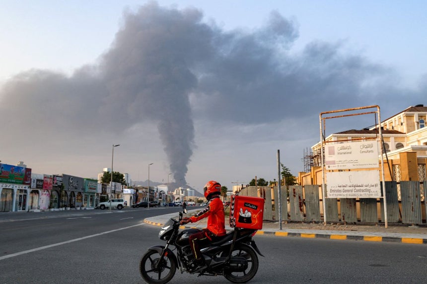 3日（現地時間）、アラブ首長国連邦（UAE）のフジャイラ工業地帯で爆発が発生した後、巨大な煙の柱が立ち上る中、配達員が道路沿いをオートバイで通過している。AFP＝聯合ニュース 