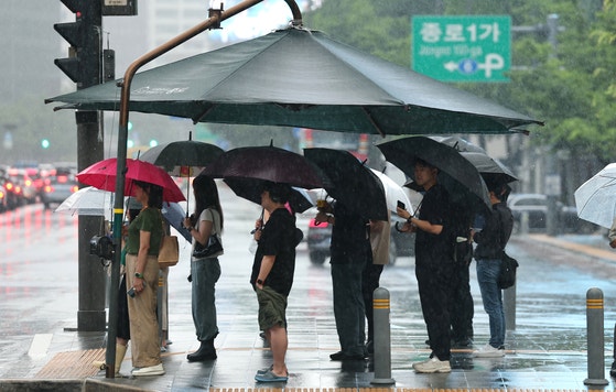 昨年6月20日、ソウル・光化門（クァンファムン）交差点で傘を差した市民らが出勤している。［ニュース1］