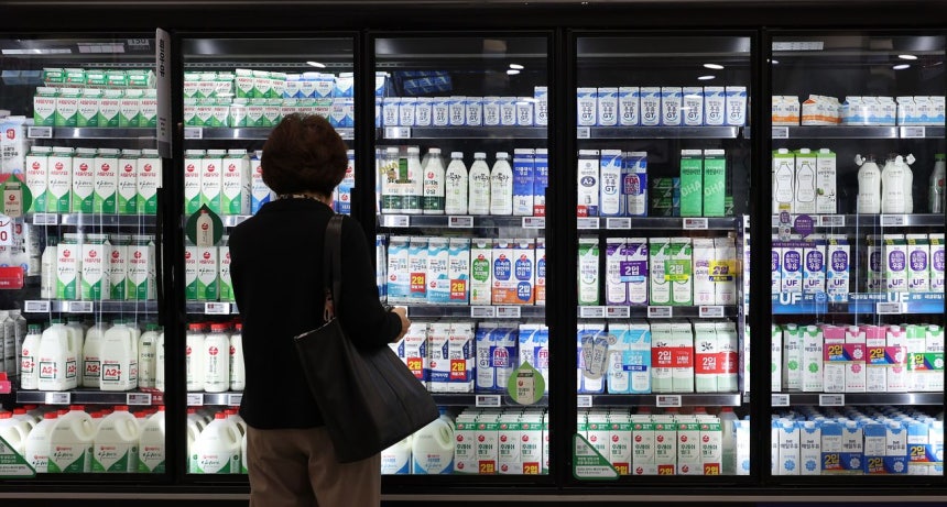 ある消費者がスーパーの牛乳コーナーを見ている。