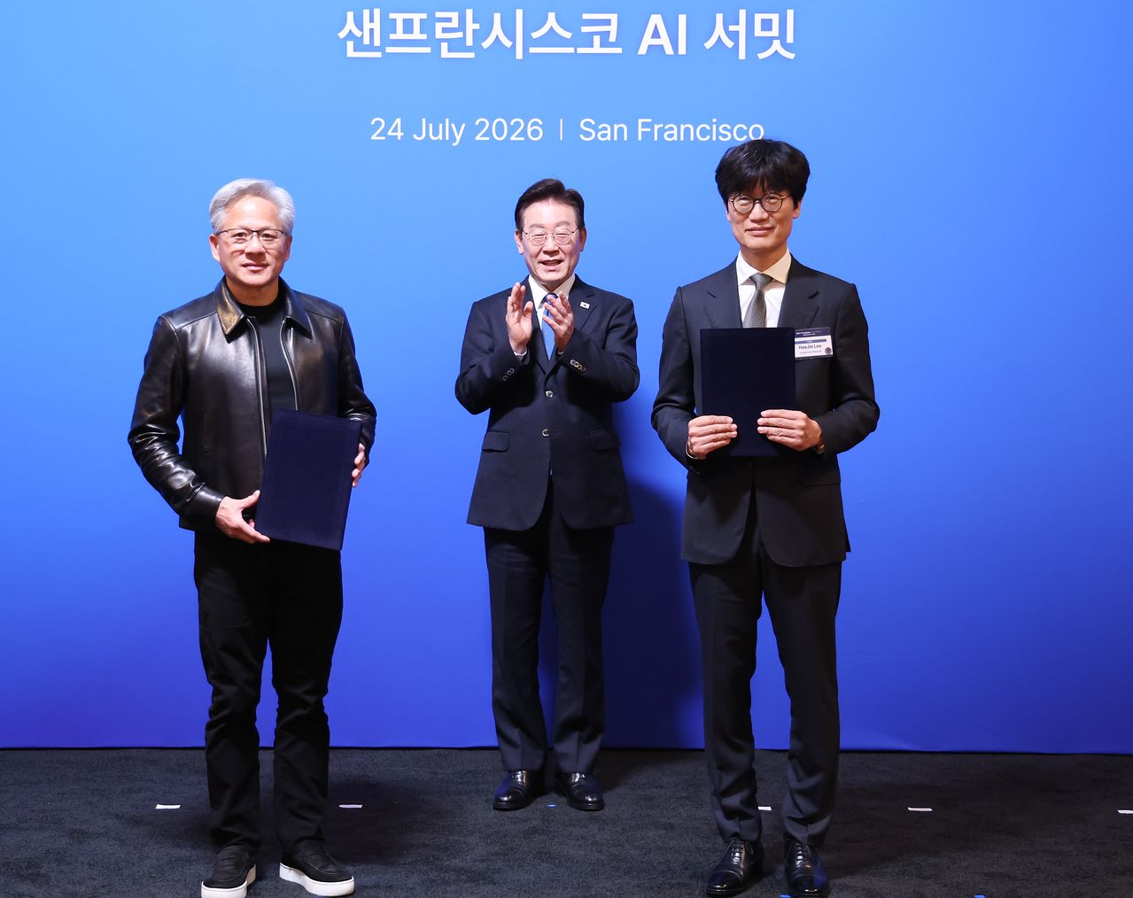 NAVERの李海珍（イ・ヘジン）取締役会議長とエヌビディアのジェンスン・フアン最高経営責任者（CEO）が24日（現地時間）、李在明（イ・ジェミョン）大統領が同席する中、米サンフランシスコの「ザ・ミッドウェイ」で開かれたAIサミットに先立ち、グローバルAIファクトリー構築に向けた持ち株投資の誘致に関する戦略的投資協約を締結した後、記念撮影に応じている。［ニュース1］