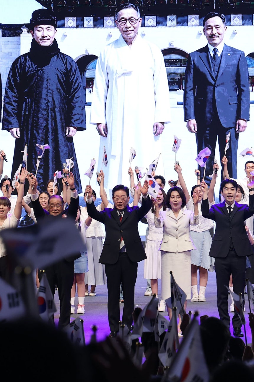 韓国の李在明（イ・ジェミョン）大統領と金恵景（キム・ヘギョン）夫人が15日、ソウル鍾路区（チョンノグ）の世宗（セジョン）文化会館で開かれた第81周年光復節（独立記念日）慶祝式典に出席し、独立有功者の子孫など国民代表と共に万歳三唱をしている。舞台のスクリーンに映っている人物はAIで再現した友堂（ウダン）・李会栄（イ・フェヨン）、白凡（ペクボム）・金九（キム・グ）、島山（トサン）・安昌浩（アン・チャンホ）先生（左から）。［聯合ニュース］