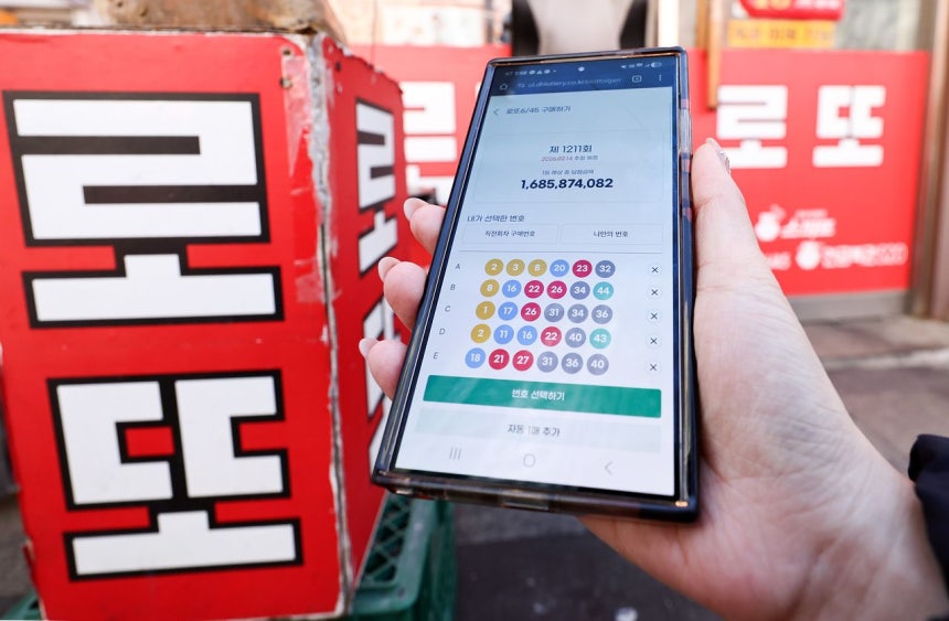 携帯電話で数字選択式宝くじ「ロト」を購入できるようになった今年2月、ソウル市内の宝くじ販売店の前で、携帯電話を使ってロトを購入する市民。［ニュース1］