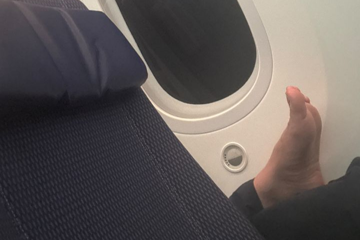  飛行機の前の座席の肘掛けに足を乗せている乗客の様子。［SNS キャプチャー］